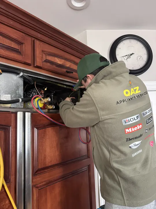 Technician working on a built-in refrigerator compressor through the top grille